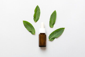 Natural Mint Essential Oil in a Glass Bottle. organic cosmetics with herbal extracts of mint on colored background