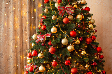 Decorated Christmas tree at home. Artificial Christmas tree with golden and red bubbles, bows, some beads, lights on it