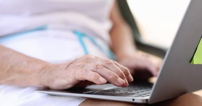 Hands of elderly woman are typing on laptop keyboard