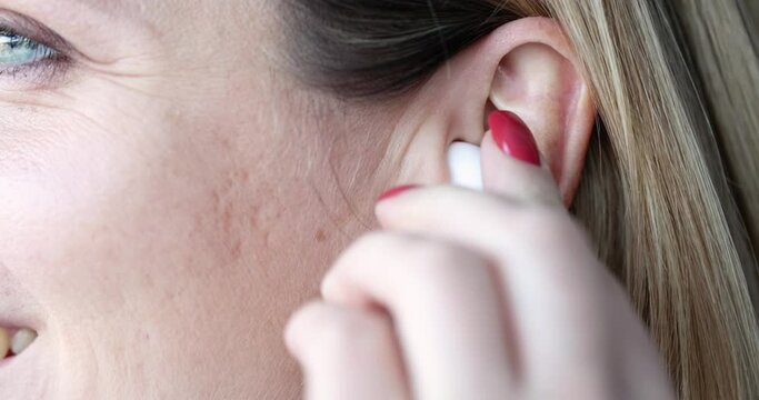 Woman inserts white wireless earpiece into ear
