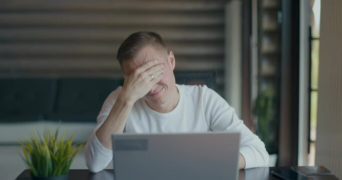 Upset young man covering face with palm in despair after reading bad news on laptop