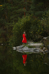 Reflection of a girl in a red dress in the lake. Against the background of a large pine forest