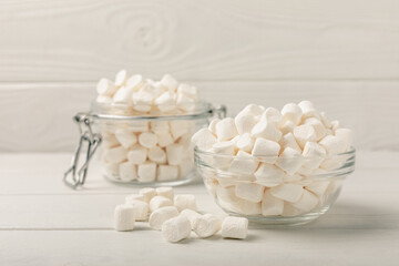 Fototapeta na wymiar Marshmallows in a glass bowl and jar on a white textured table.Sweets and snacks for a snack.Chewy candy close-up.Copy space.Place for text.
