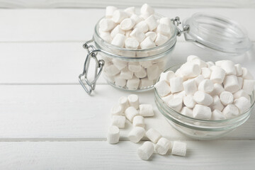 Marshmallows in a glass bowl and jar on a white textured table.Sweets and snacks for a snack.Chewy candy close-up.Copy space.Place for text.