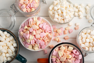Many different marshmallows in bowls and jars on a white textured wood. White and fruit marshmallow. Sweets and snacks for a snack. Chewing candies close-up. Copy space. Place for text.