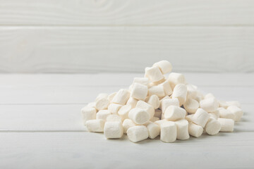 Fototapeta na wymiar Loose white marshmallows on white texture wood.Sweets and snacks for a snack.Chewy candy close-up.Copy space.Place for text.