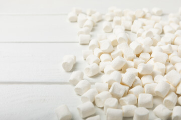 Fototapeta na wymiar Loose white marshmallows on white texture wood.Sweets and snacks for a snack.Chewy candy close-up.Copy space.Place for text.