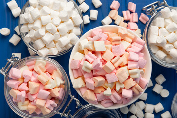 A lot of different marshmallows in bowls and jars on a blue textured wood. White and fruit marshmallows.Sweets and snacks for a snack.Chewy candy close-up.Copy space.Place for text.