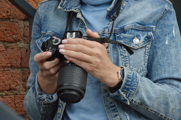 Women's hands are holding a camera. A girl in a denim jacket looks through pictures on a professional camera. Close-up.