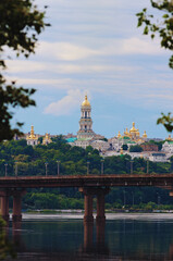 Summer landscape of famous Kyiv's green hills. Scenic landscape view of ancient Kyiv Pechersk Lavra. It is a historic Orthodox Christian monastery. Tree leaves border. Natural frame. Cloudy sky