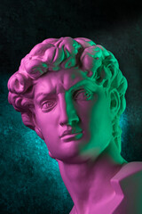 Gypsum copy of head statue David in bright neon colors for artists on a dark background. Face...