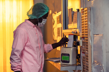 African quality control employee man in sterile suit clock in with time clock system of factory policy before working in processing warehouse