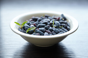 Haskap berry with fresh green leaves in white bowl on wooden table. Honeyberry (Lonicera caerulea)