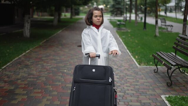 Little woman pulling heavy big travel bag in slow motion on city street. portrait of confident Caucasian brunette little person with luggage outdoors