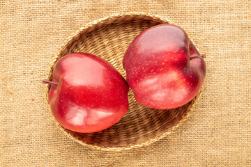 Two ripe red apples in a straw plate on burlap, close-up, top view.