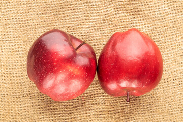 Two ripe red apples on burlap, close-up, top view.