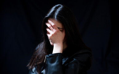 Young woman in a black leather jacket, sad and lonely in a dark room. Depression and grief