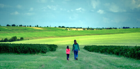 Back view of two young girls sisters walking in the green field.  Freedom, nature, happiness and healthy lifestyle concept.