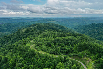 Fototapeta premium Road Winds through Green Mountains Under Blue Sky and Puffy Clouds