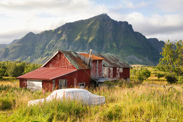 Abandoned house on one of the many islands of Lofoten, Norway, with an old covered-up car standing...