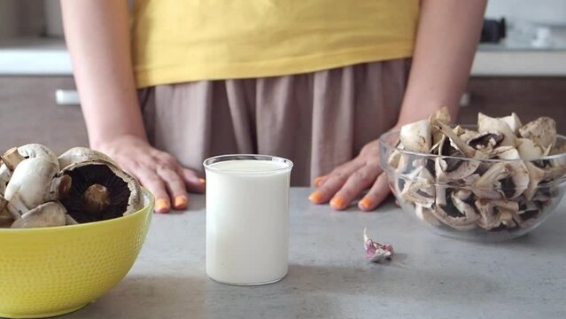 Woman cut mushrooms in champignons, prepared cream, milk and garlic to make cream soup, mashed soup or pasta sauce. Close up HD. Cooks lunch or dinner. Healthy protein vegetable food. Brown and yellow