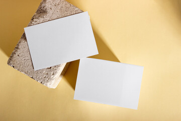 Mockup with blank horizontal paper cards with copy space on a plinth with palm leaves. Hard sunlight and shadows on a beige background. Minimal template for business layout. Top view, flat lay