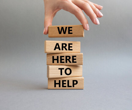We are here to help symbol. Concept words we are here to help on wooden blocks. Beautiful grey background. Businessman hand. Business and we are here to help concept. Copy space.