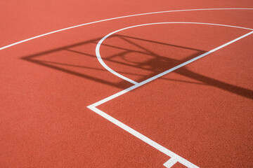 Shadow of the rack with shield and basketball ring on orange basketball rubber field ground during sunny day outdoors. Basketball game background