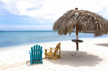 Two wooden beach chairs under thatched roof, Aruba