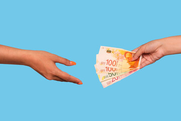 Hand giving israel shekels and hand take, over blue background. Giving money to help