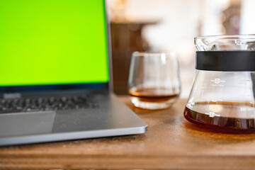 Cozy cafe atmosphere with a glass of coffee, carafe and a laptop with a green screen on the wooden table