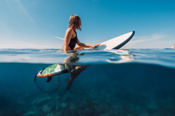 Sporty surf girl in bikini sitting on surfboard, split view in ocean - obrazy, fototapety, plakaty