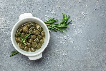 Marinated capers with fresh rosemary in a small bowl, on light wooden background. Long banner...
