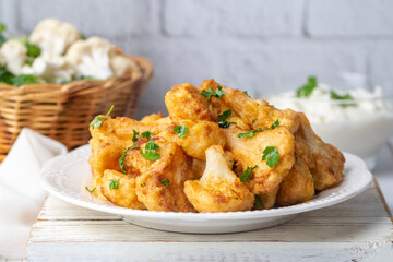 Fried in batter Cauliflower florets served on a black plate on a grey concrete table with...