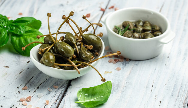 Capers. Marinated or pickled canned capers fruit with fresh rosemary in a small bowl, on gray background. place for text, top view