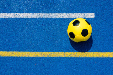 Colorful sports court background. Top view light blue field rubber ground with white and yellow lines and yellow soccer ball on sunny day outdoors