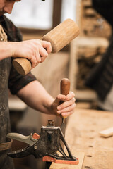 Vertical of cropped man hands, master carpenter using wooden mallet and chisel in repair shop, loft...
