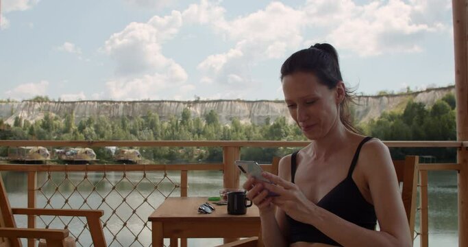 Woman comunicate by smartphone with friends while resting on lake on weekend
