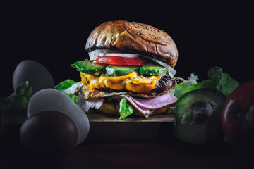 Deliciosa hamburguesa con vegetales, jamón, queso y huevo rodeada de ingredientes