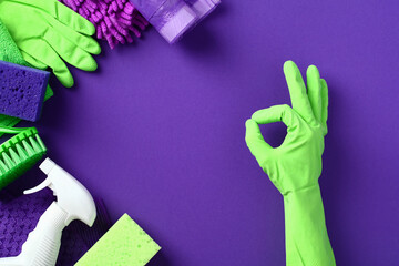 Female hand shows OK gesture over purple background with cleaning supplies and chemicals.