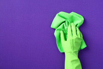 Female hand in green protective glove with green rag over purple background. House cleaning service...