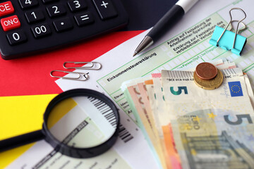 German income tax return form with pen and european euro money bills lies on flag close up....