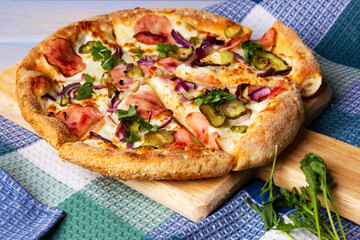 Bacon Pizza with pickled cucumbers and onion on wooden cutting board.