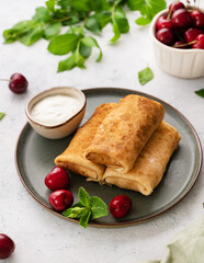 Delicious homemade pancakes or crepes  with fresh cherries and sour cream on a dark plate on a light  background close up