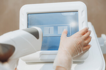 The beautician's hand presses the buttons on the device for laser hair removal. Close-up.Skin care...