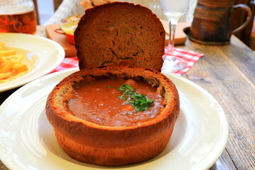 Original dish - goulash soup in bread pot, plate in restaurant, cafe. Delicious hearty meat dish of Czech, Bulgarian, Romanian cuisine, European recipe. Prague