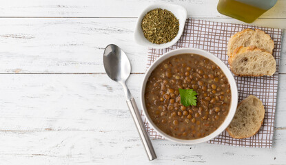 Brown lentil soup in a bowl with bread slices and seasoning over wooden table with copy space
