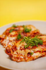 Lasagne on a white plate on a yellow background