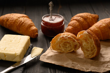 Freshly baked croissants with berries jam and butter, dark wooden background, selective focus