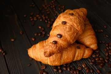 Croissants with coffee beans on a wooden background.